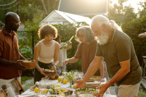 Young and senior couples in casualwear putting cooked homemade food on table while preparing for family dinner in natural environment