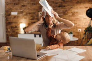 Stressed hoa board member and mother covering her head with paperwork while her small son is offering her a cookie at home.