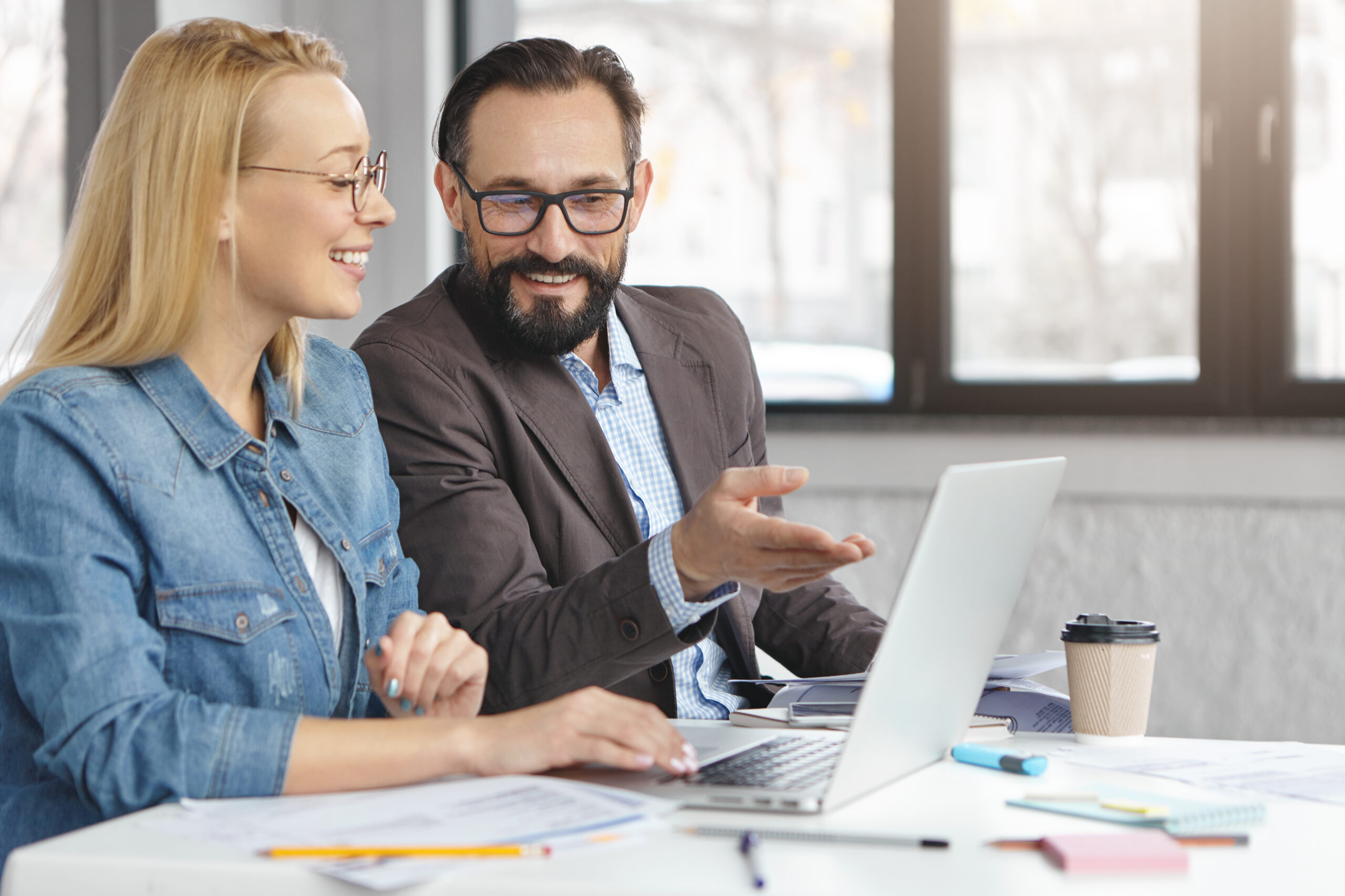 Experienced mature male community manager explains amending government documents to young board member, shows information on laptop computer has pleased expression, glad to work and collaborate together.